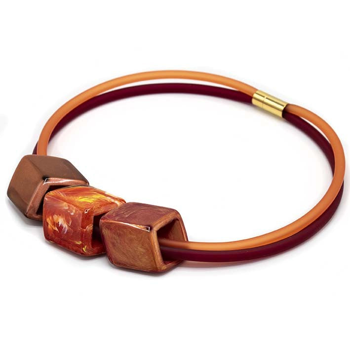 Ketting met 3 Cubes in warme tinten oranje, rood en koper aan rode rubber ketting met goudkleurige sluiting, zijaanzicht.