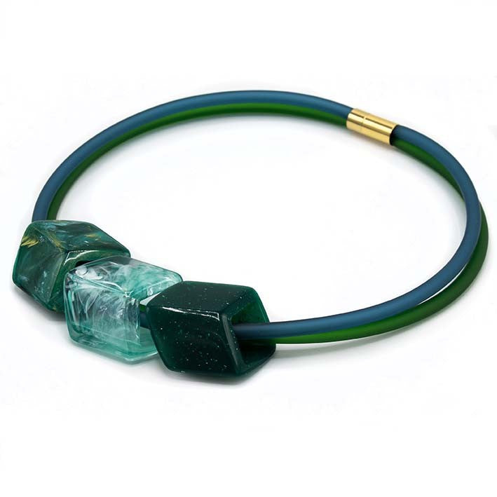 Ketting met 3 Cubes in groentinten (smaragd, mint, donkergroen) aan blauw-groene rubber ketting met goudkleurige sluiting, zijaanzicht.